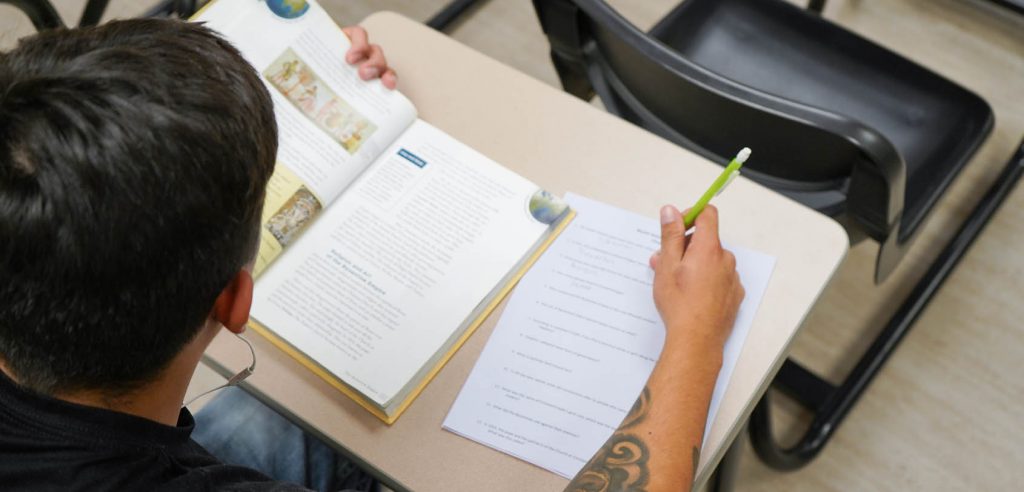 A learner taking notes beside an open study book
